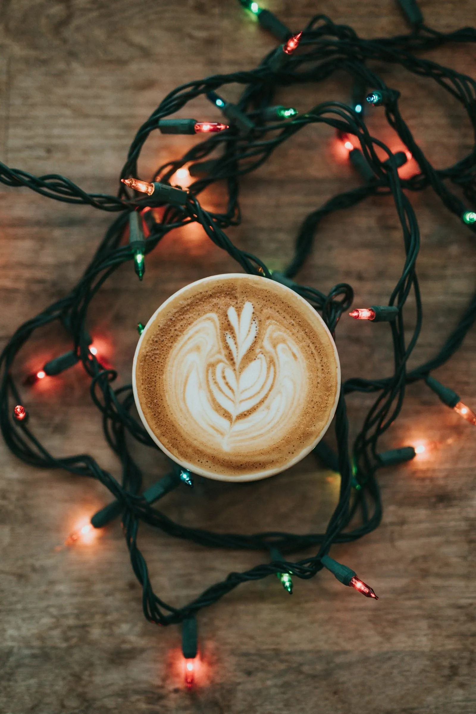 Latte with heart latte art next to a tangle of glowing string lights on a wood table