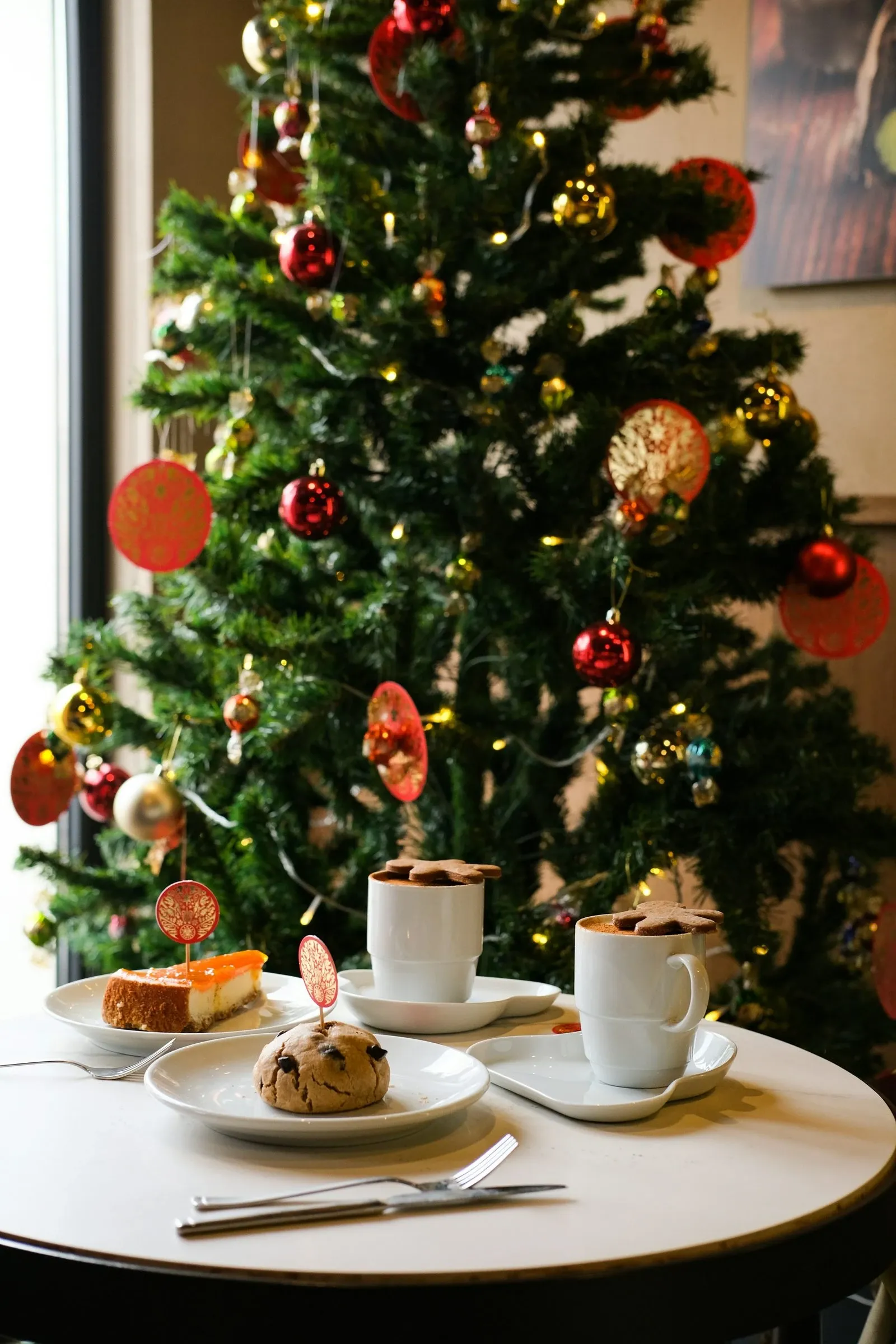 Small table beside a Christmas tree set with coffee, cookies and holiday treats