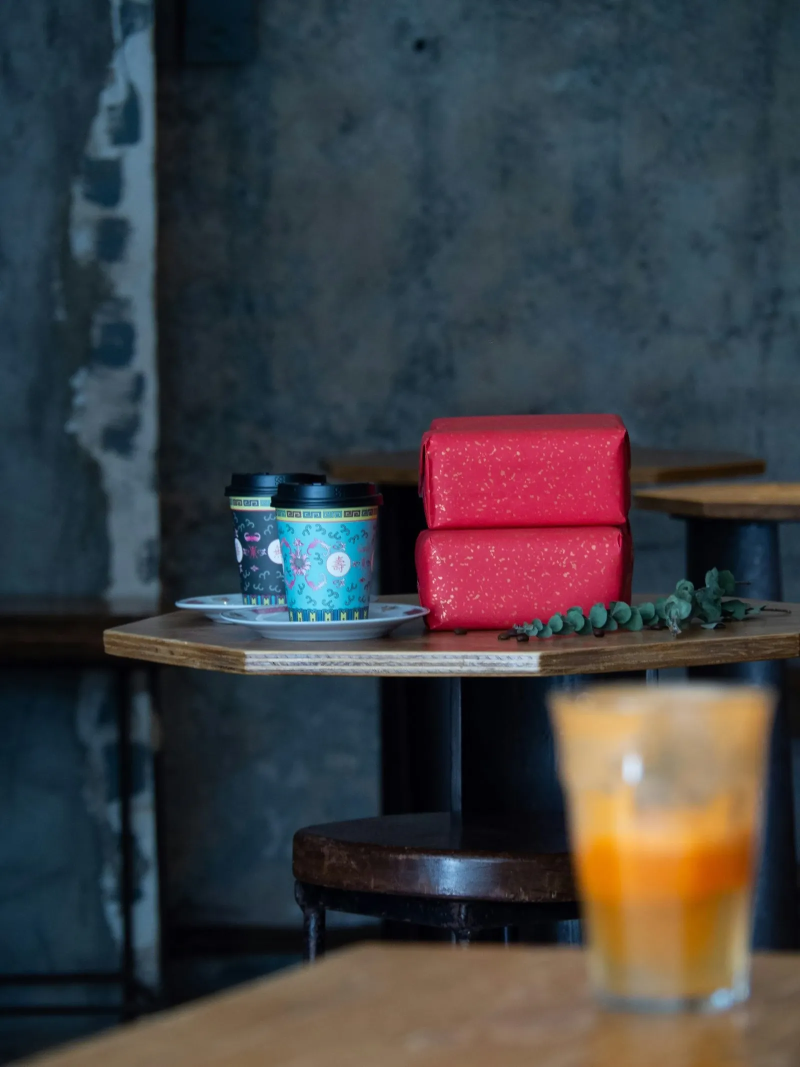 Two coffee cups on a saucer beside stacked red gift boxes on a dark cafe table