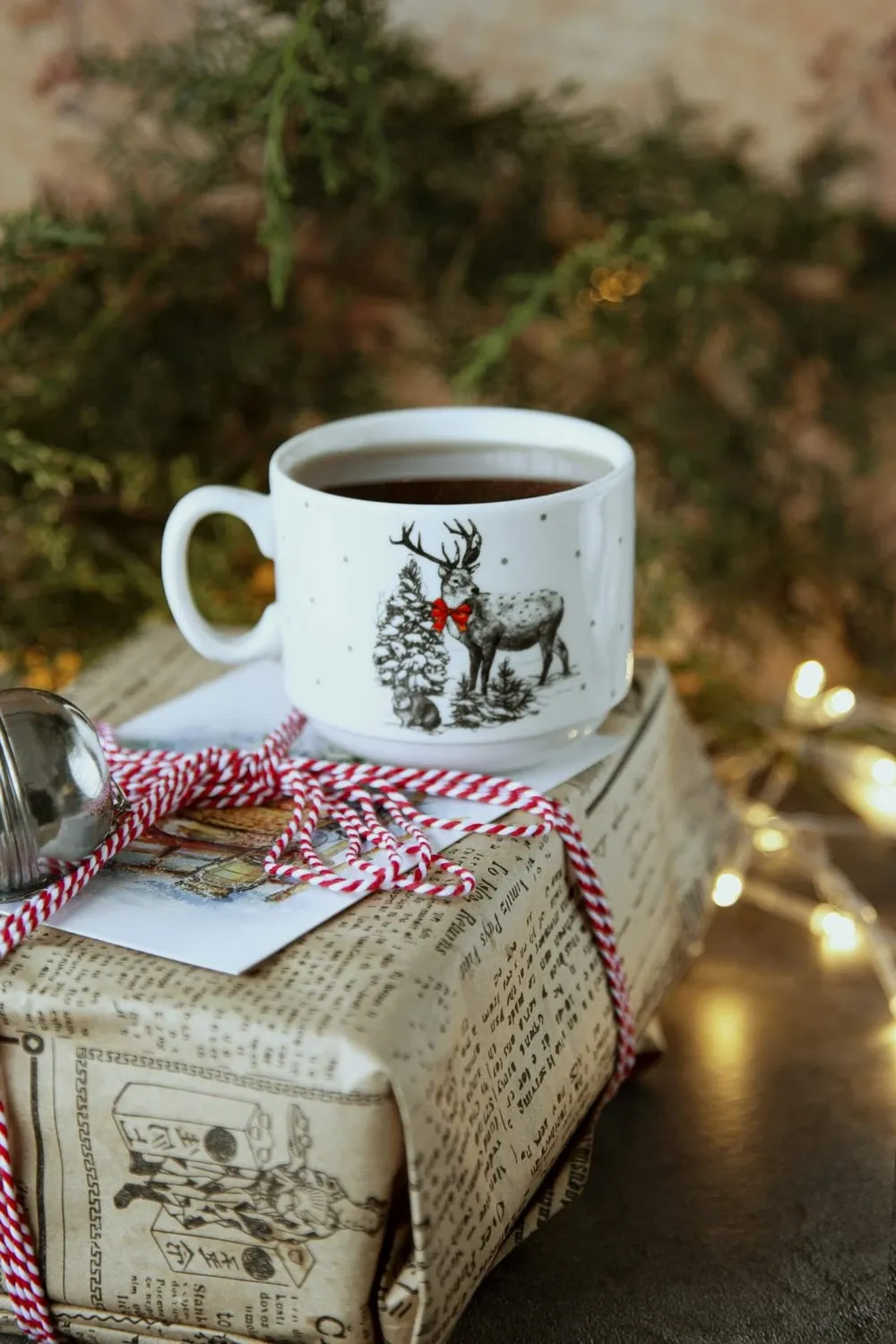 White mug of coffee with a reindeer print sitting on a wrapped present tied with red and white twine