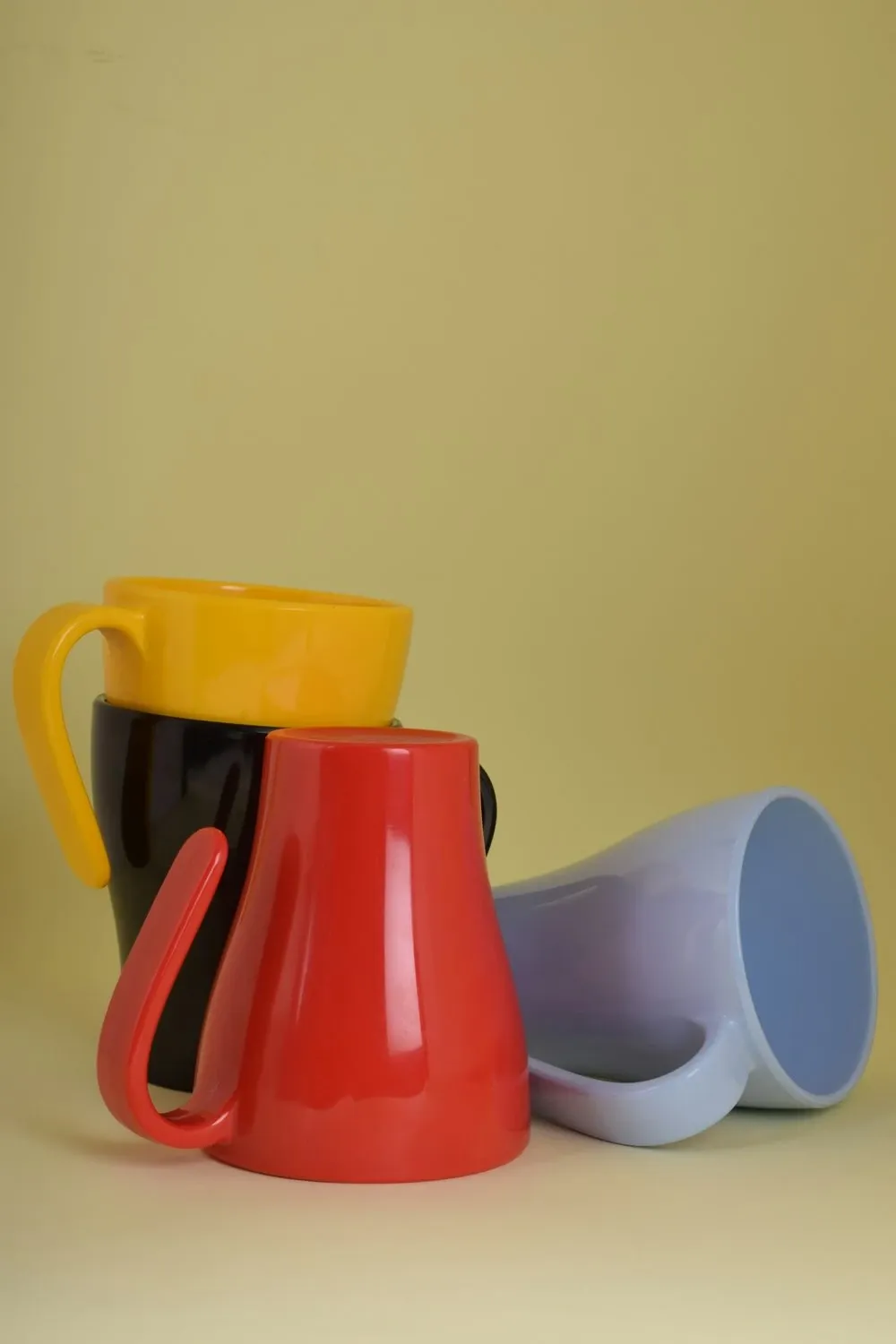 Yellow mug, red jug and lilac cup in bright glazes grouped on a soft yellow background
