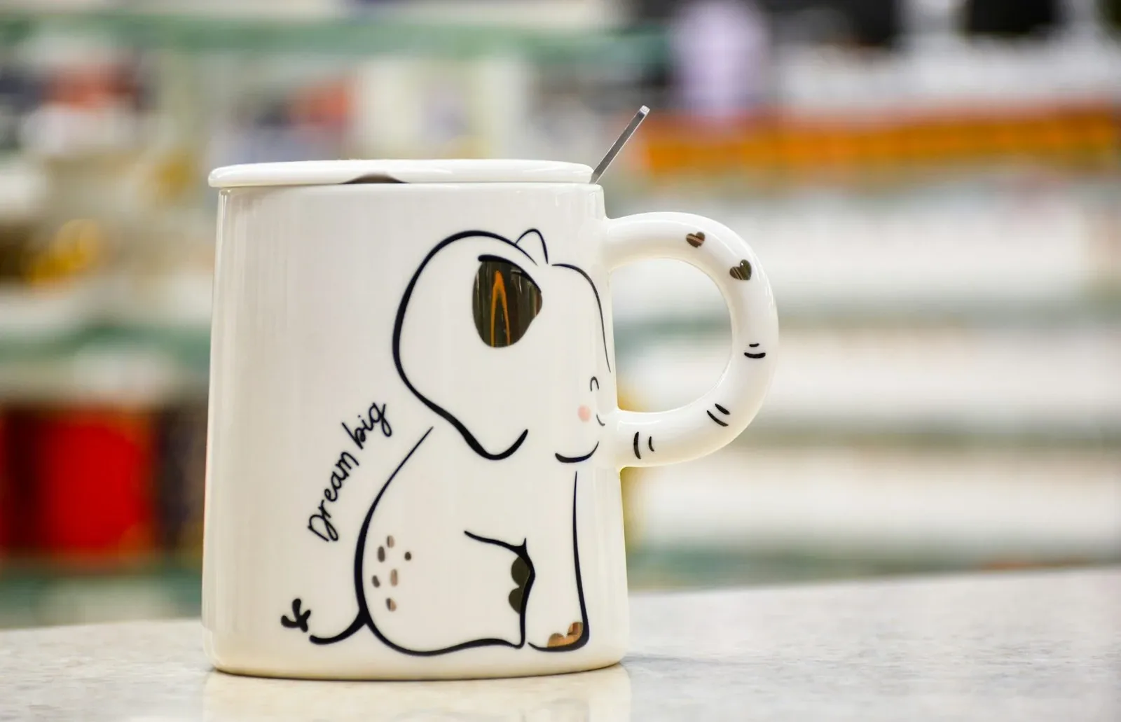 White coffee mug with a simple line drawing of a dog and a handwritten caption on a café counter