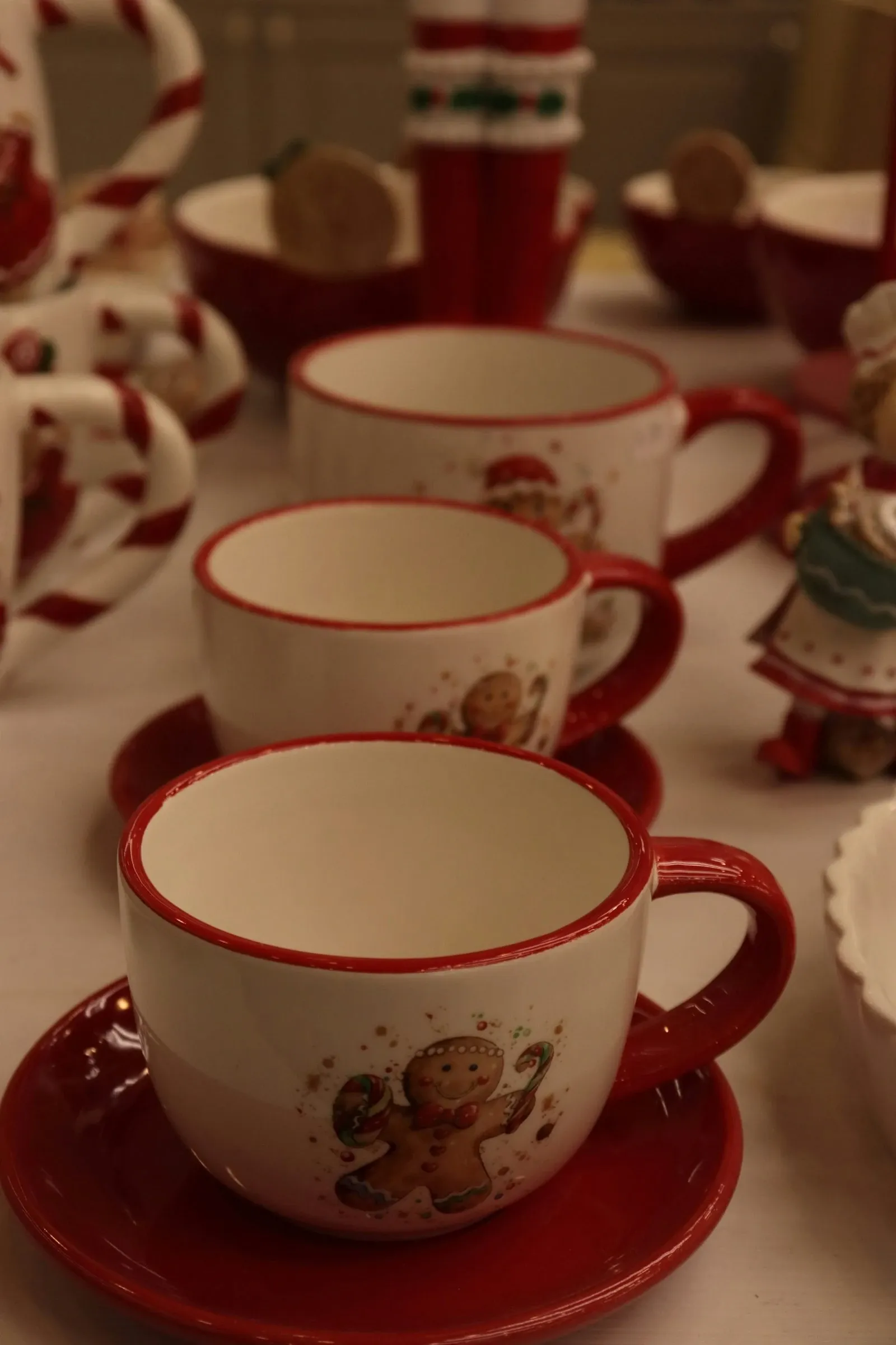 Red and white gingerbread man mugs and saucers stacked on a table with holiday decor