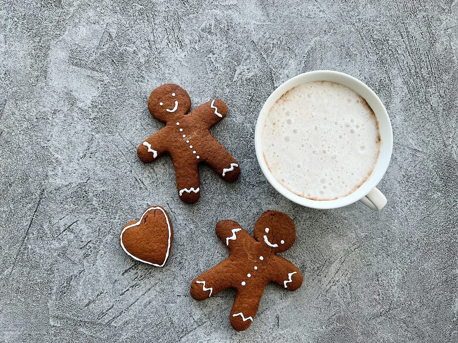 Cup of milky coffee on a gray surface beside three gingerbread man cookies