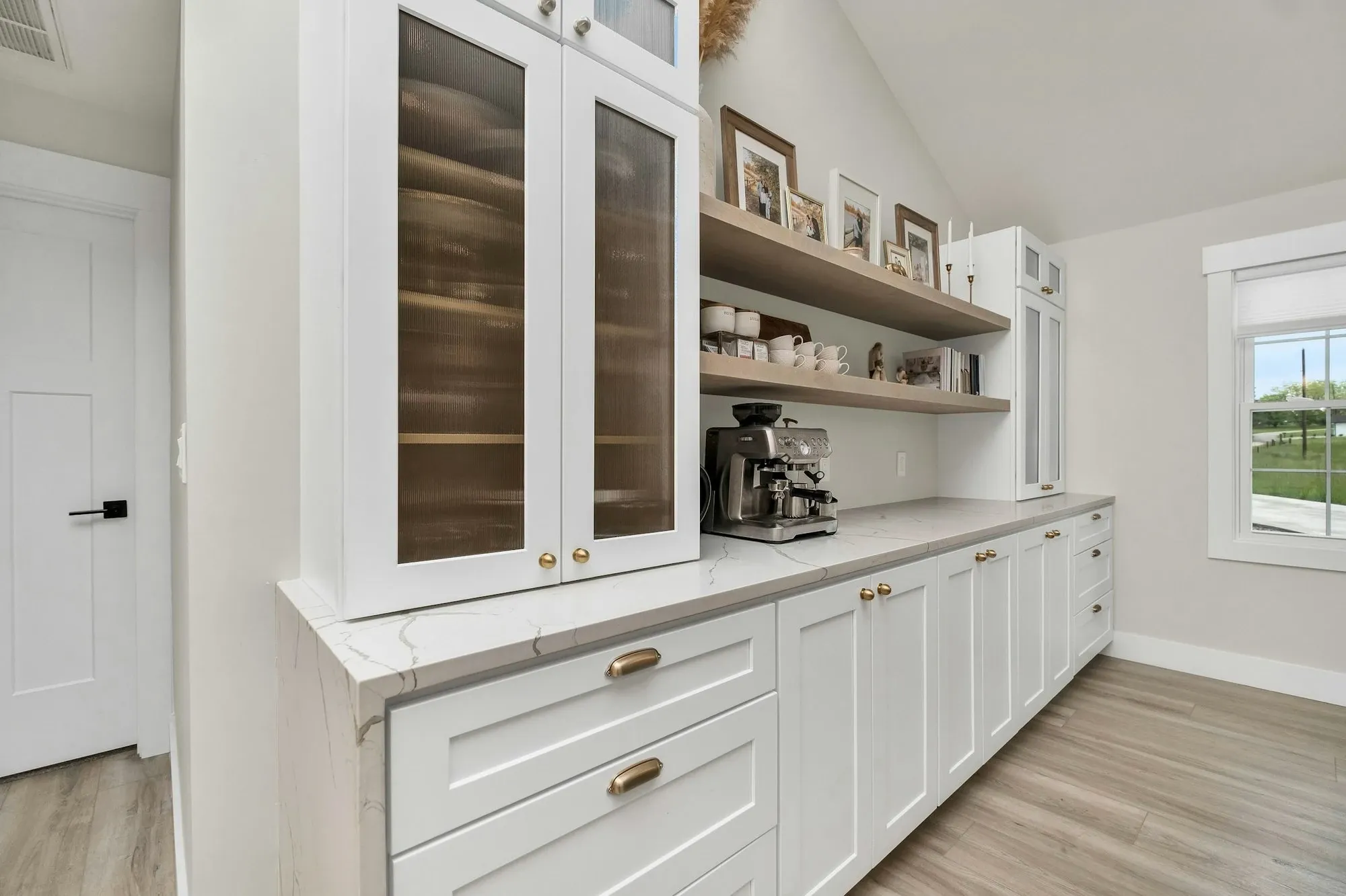 Home coffee station corner with white cabinets, open shelves and a coffee maker on the counter