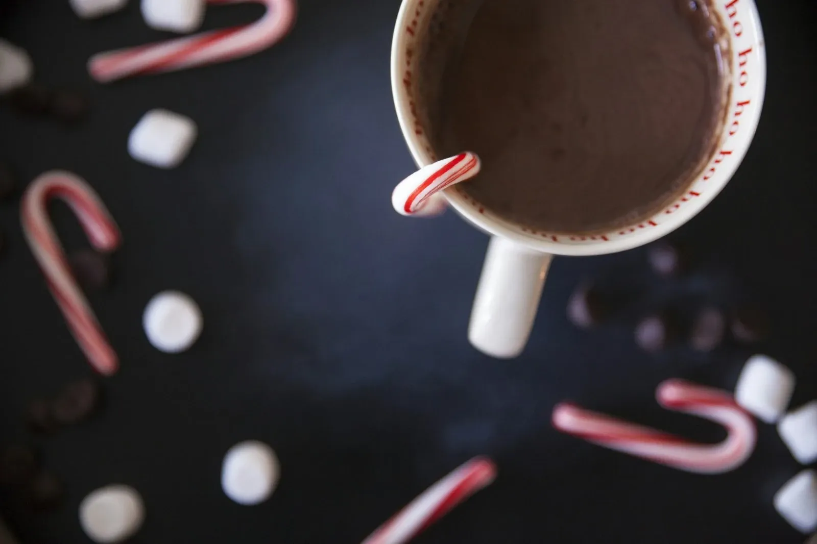 Mug of hot chocolate seen from above on a dark table scattered with mini candy canes and marshmallows