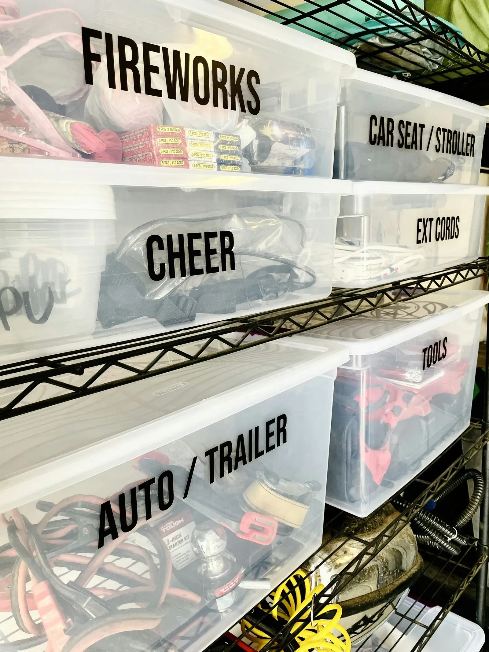 Clear plastic storage bins with large black labels stacked on a metal wire shelf