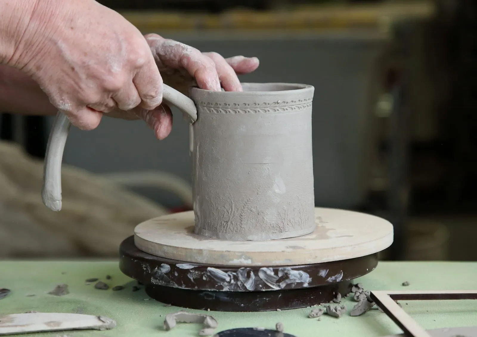 Hands attaching a clay handle to a handmade mug on a pottery wheel