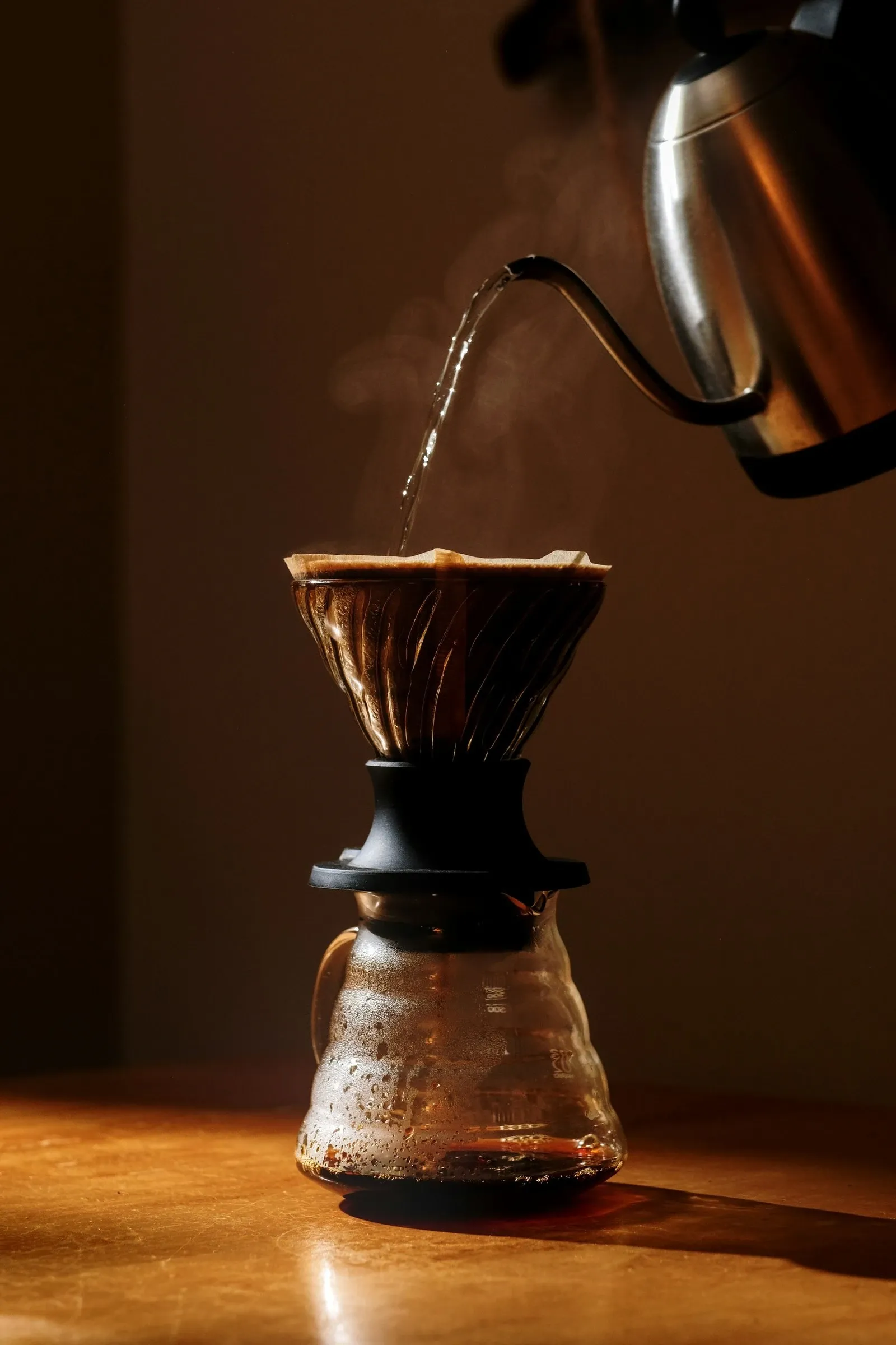 Gooseneck kettle pouring water into a pour-over dripper set on a glass coffee server