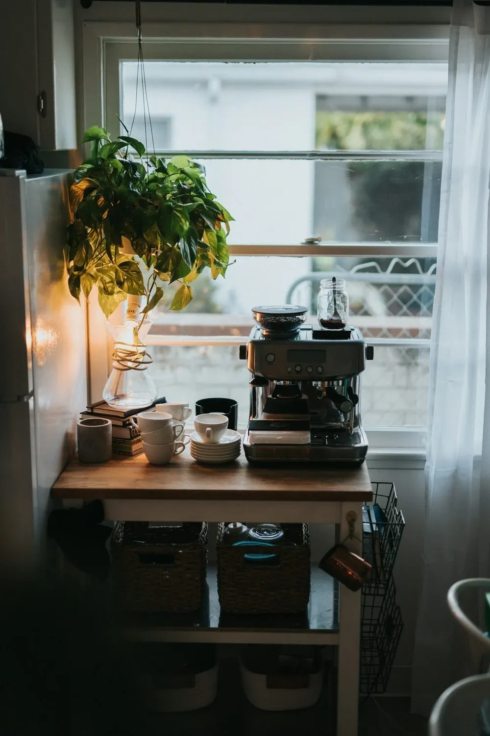 Rolling wooden coffee bar cart with an espresso machine by a window