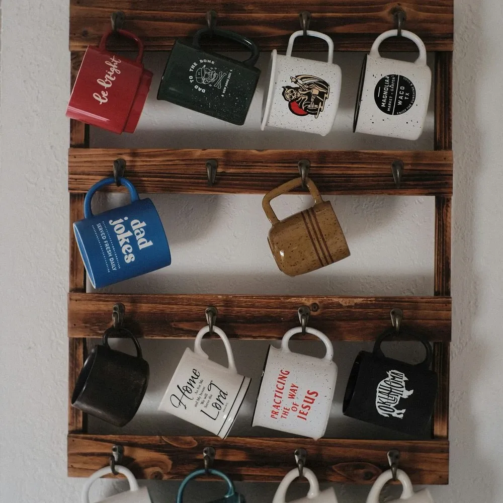 Dark wood wall rack with hooks holding a mix of white, red and blue coffee mugs